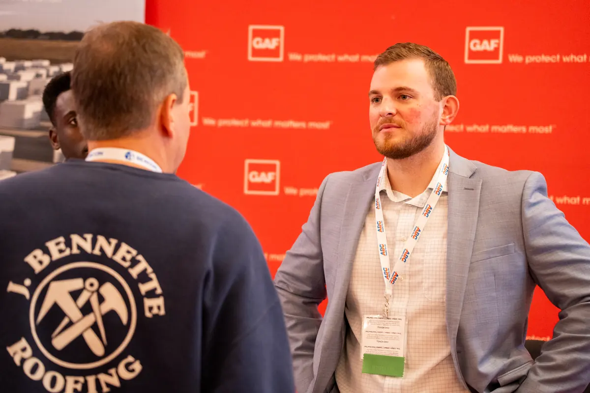 An exhibitor talking with roofing contractors at a booth on the NERCA trade show floor